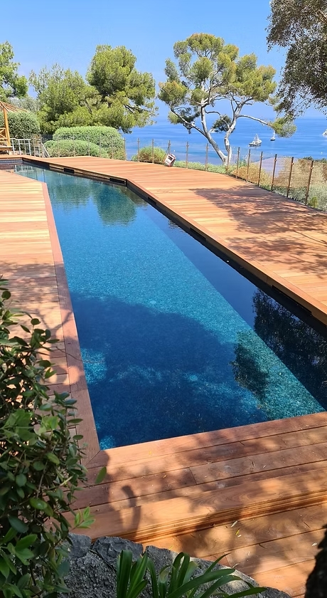 Couloir de nage sur mesure | Piscine vue mer et terrasse bois Couloir de nage étroit bordé d'une terrasse en bois clair. Vue imprenable sur la Méditerranée, ciel bleu et végétation luxuriante.