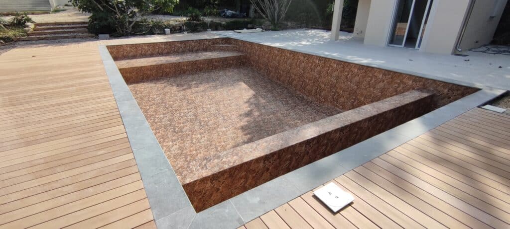 Piscine rectangulaire vide avec liner effet pierre marron et terrasse en bois naturel en cours de construction.