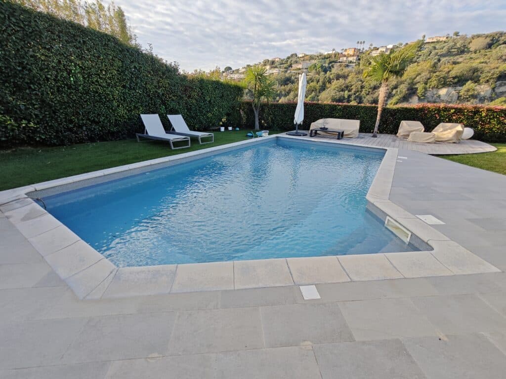 Piscine rectangulaire avec terrasse en pierre, transats et vue panoramique sur les collines environnantes.