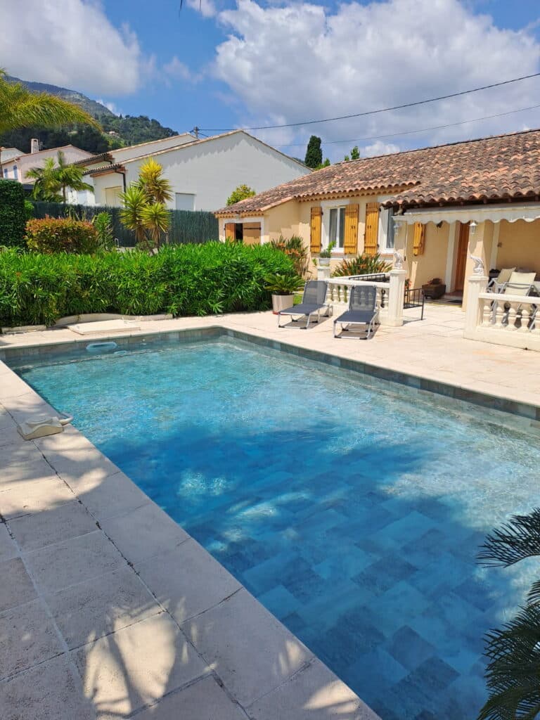 Villa avec piscine et jardin méditerranéen ensoleillé Piscine bleue devant une villa avec jardin méditerranéen et vue sur la montagne par une journée ensoleillée.