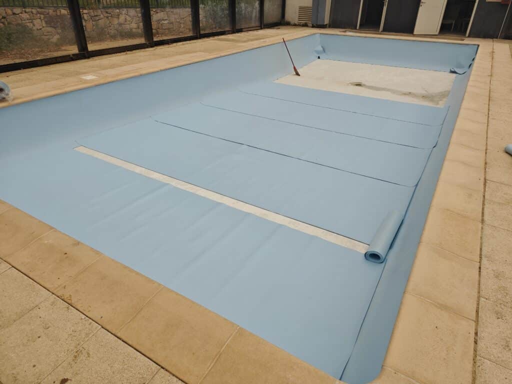 Pose d'un liner bleu ciel dans une piscine rectangulaire en cours de rénovation.