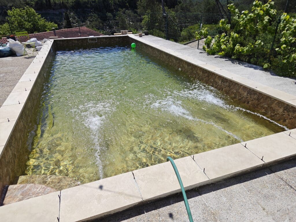 Piscine à l'eau jaunâtre avec jets d'eau actifs et bordure en pierre.